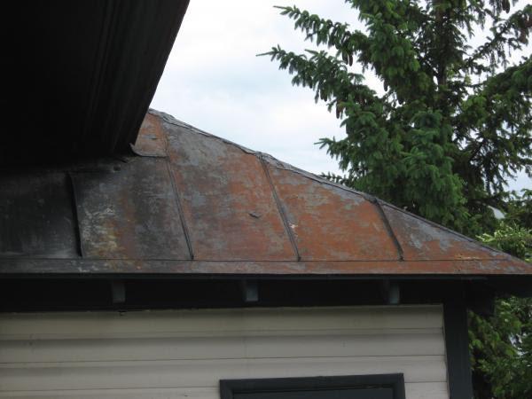 Roof of covered balcony on west side of building showing rusting metal surface and patched seams